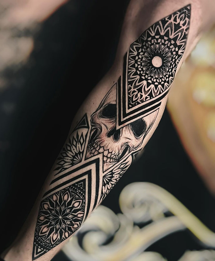 A detailed forearm tattoo combining a realistic skull with intricate geometric patterns and mandala designs, presenting bold and unique tattoo ideas for men.