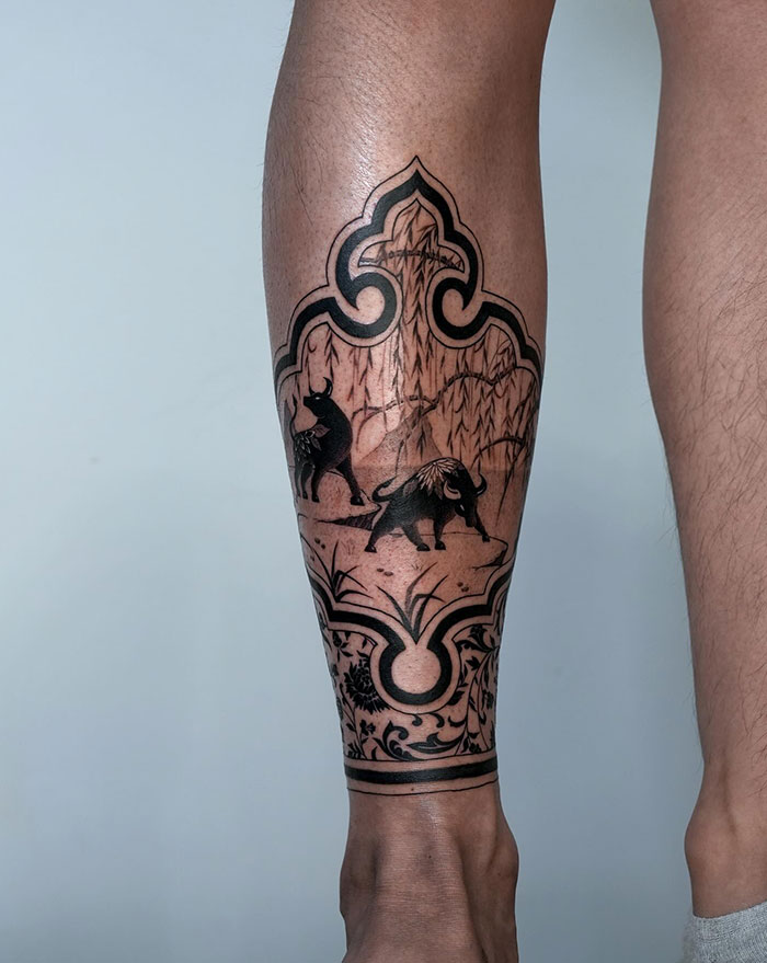  A calf tattoo featuring two detailed buffalo silhouettes against a stylized mountain landscape framed in a decorative pattern, offering unique tattoo ideas for men.