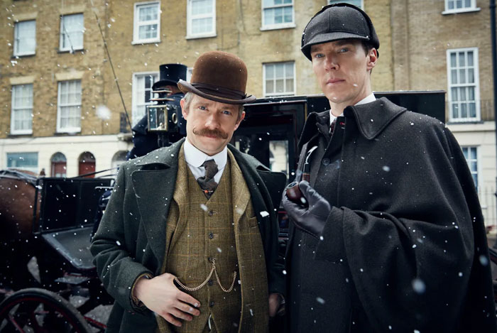 Two iconic fictional duos in Victorian attire during a snowy scene, standing in front of a carriage.
