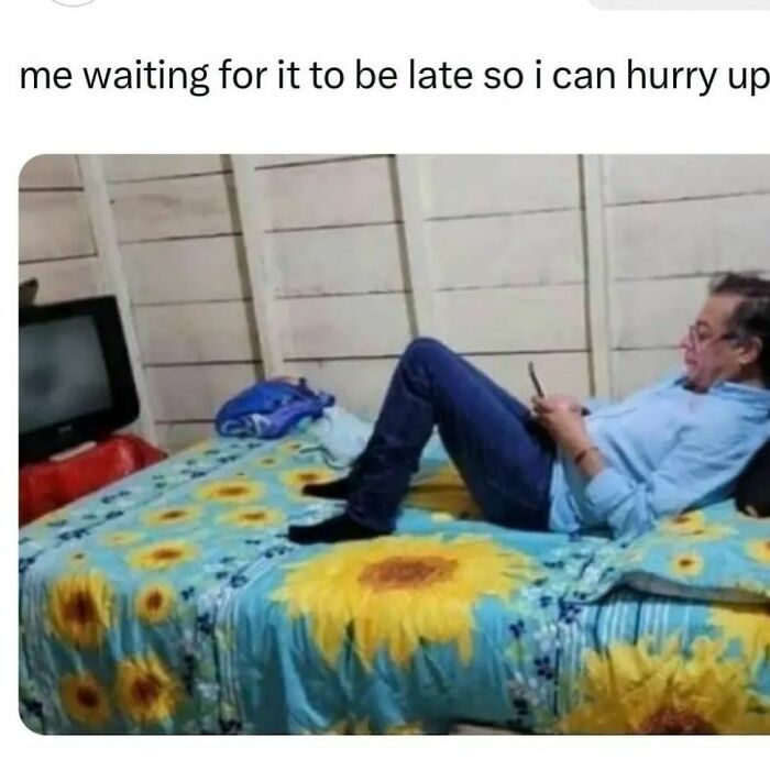 Man lying on a sunflower-patterned bed, looking at his phone, capturing a moment from hilarious memes collection.