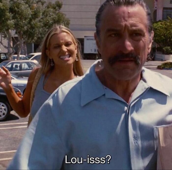 Man in focus walking, woman in background making a playful face. Scene captures a wild and wholesome '90s moment.