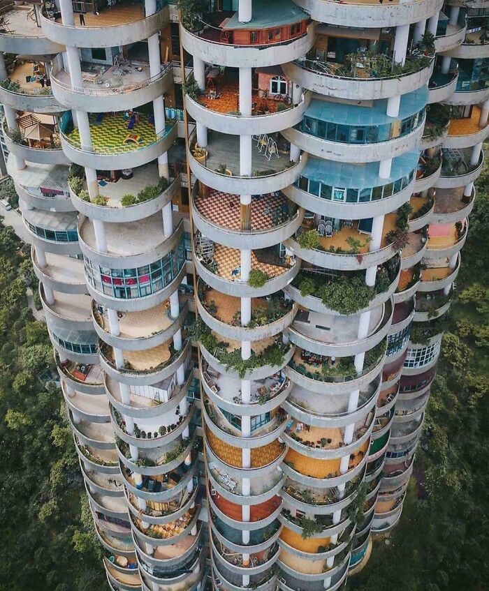 Unique bizarre building with circular balconies featuring diverse colorful designs and greenery in a lush environment.