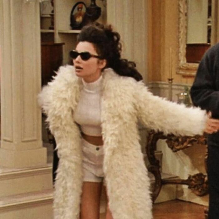 90s fashion moment: person in white fur coat and sunglasses indoors, embodying a wild, stylish vibe.