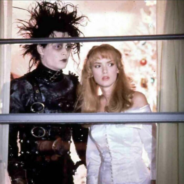 Two characters from the '90s film in a Christmas scene, one in a black outfit, the other in a white dress.