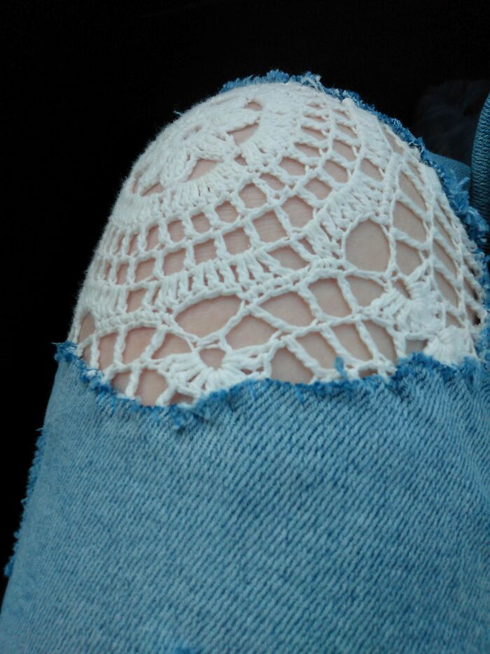 Denim jeans visibly mended with white crochet lace patch, creatively repairing and enhancing the ripped area.