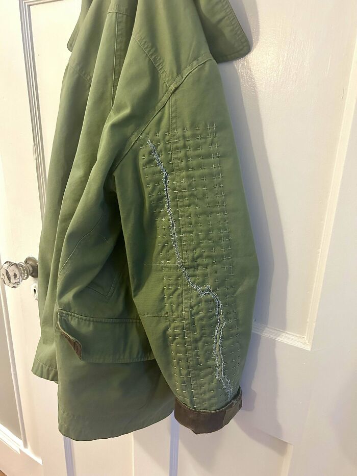 Green jacket with visible mended tear using decorative stitch patterns to make it look cooler and unique.