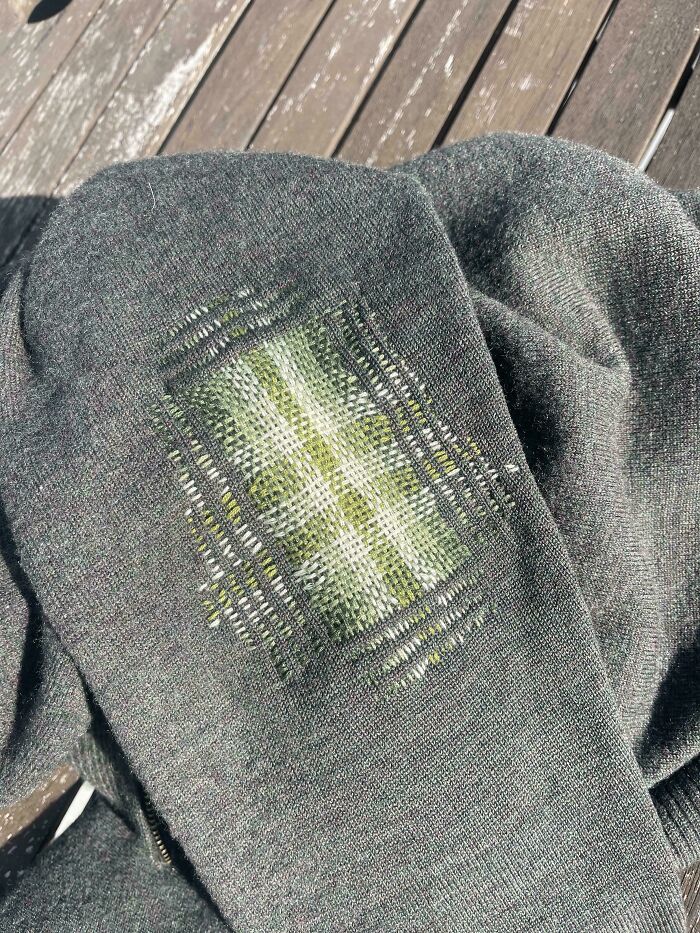 Visible mending on a gray fabric with green and white threadwork, creatively repairing a worn-out patch on clothing.