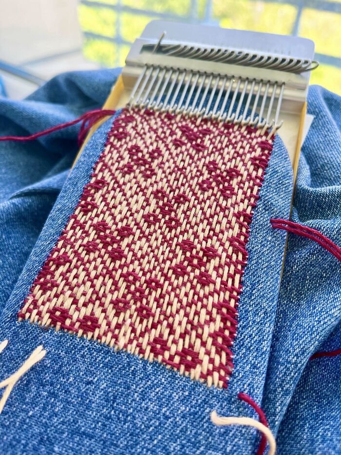 Denim visibly mended with creative red and beige embroidery using a small weaving tool, making it cooler and unique.