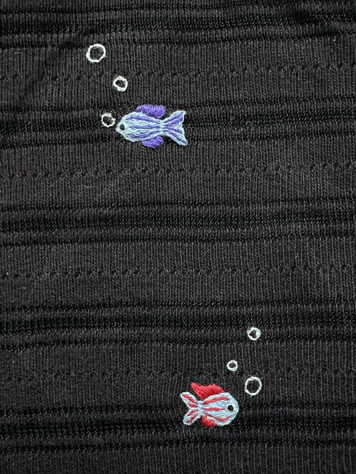 Visible mended fabric with creative embroidery of two colorful fish and bubbles, making the repair cooler.