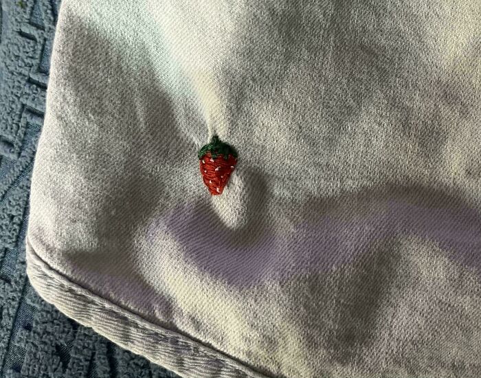 Small fabric hole visibly mended with a cute embroidered strawberry patch, creatively making it cooler.
