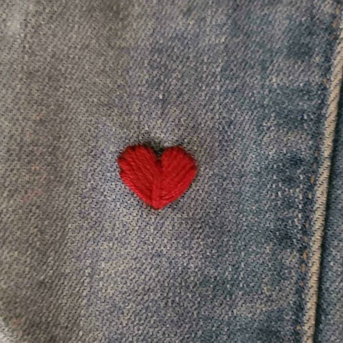 Close-up of denim fabric with a small red heart-shaped visible mend making the ruined area cooler and decorative.