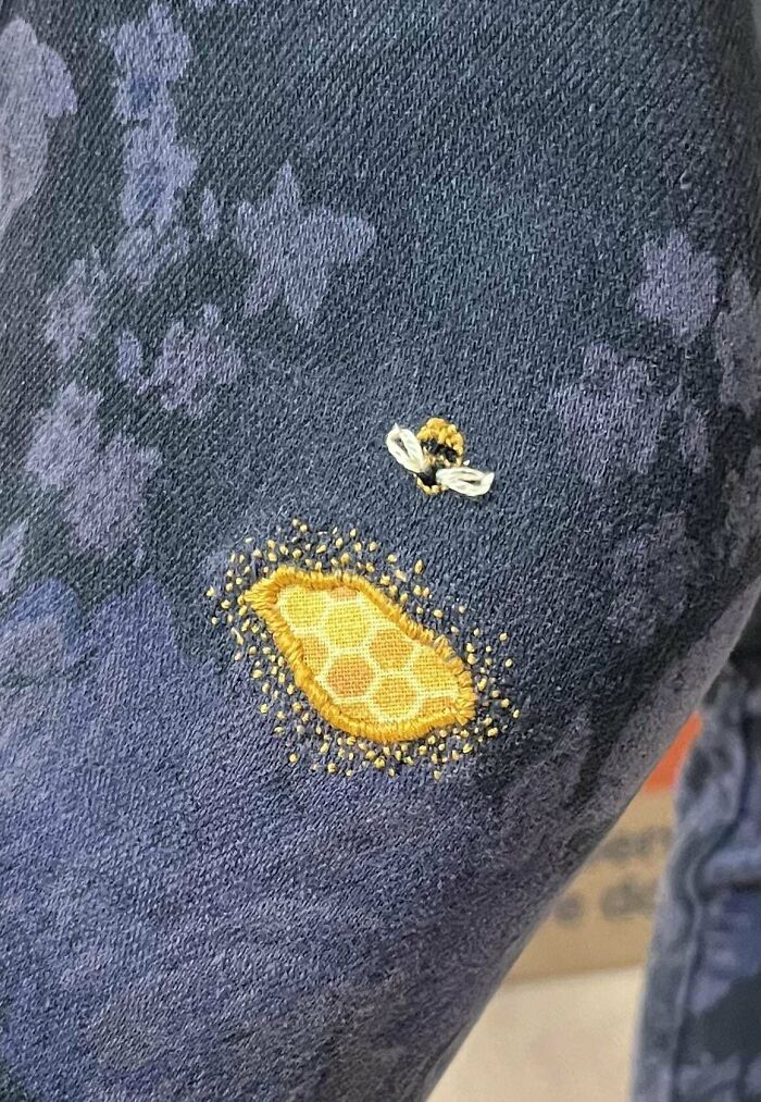 Visible mended fabric with decorative bee embroidery and honeycomb patch on dark patterned cloth.