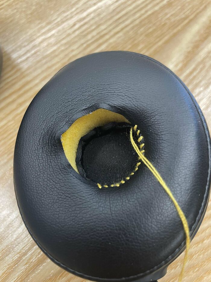 Close-up of a headphone ear pad visibly mended with yellow thread, showcasing creative and cool repairs.