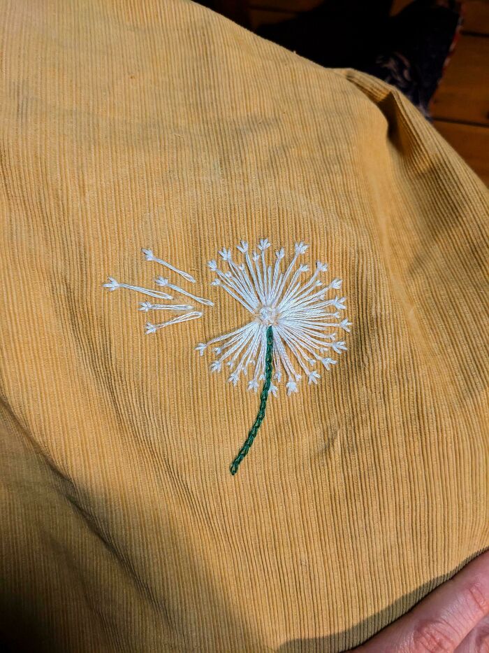Visible mended fabric with hand-embroidered dandelion design adding a cooler, creative touch to ruined clothing.