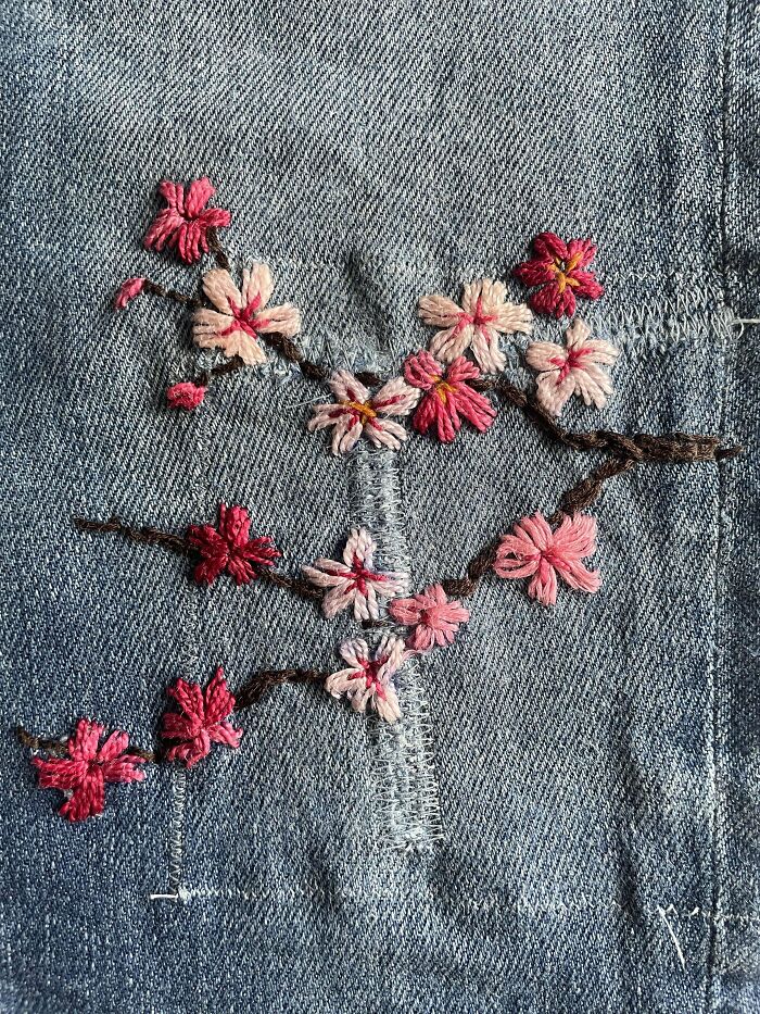 Denim fabric visibly mended with embroidery of pink and red flowers, creatively enhancing the worn area.