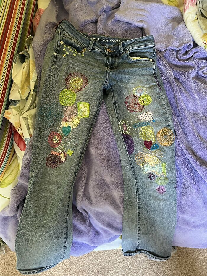 Denim jeans visibly mended with colorful, creative embroidery patches, showcasing unique and cool clothing repair.
