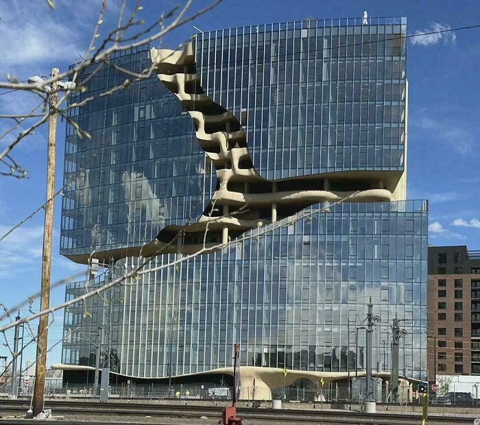 Modern bizarre building with unique curved glass facade and open staircases under clear blue sky.