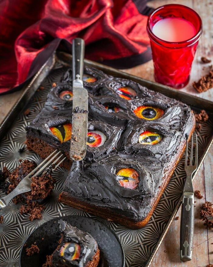 Halloween snacks featuring a chocolate cake decorated with realistic edible eyes on a patterned tray with a glass of milk.