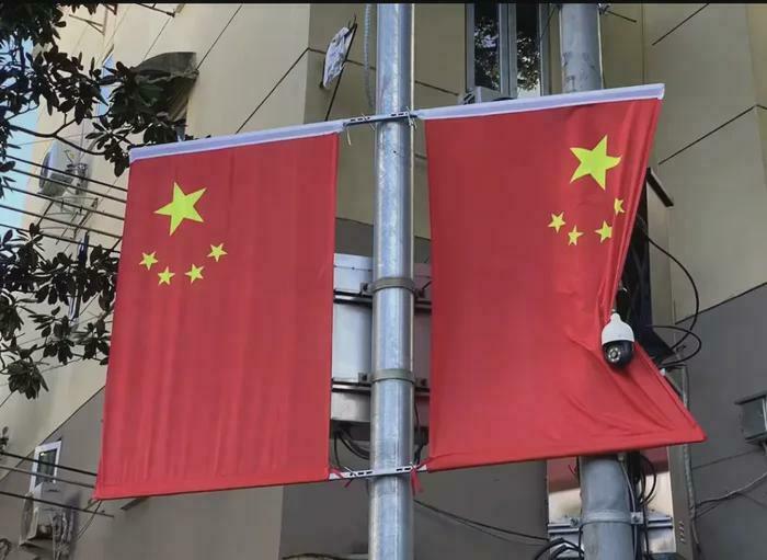Two Chinese flags on a pole, with one partially covering a surveillance camera.