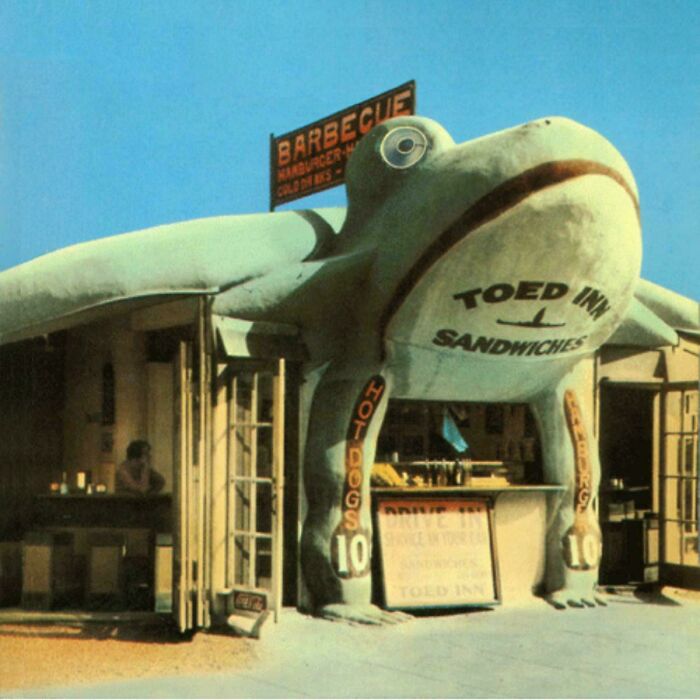Bizarre building shaped like a giant frog serving hot dogs and sandwiches at a roadside barbecue stand.