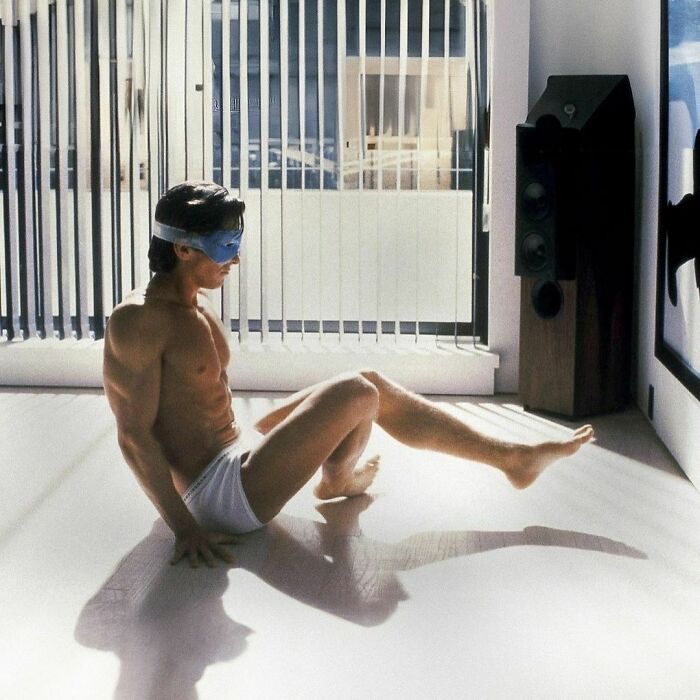 Man exercising in white shorts and a blue headband in a bright room; reminiscent of '90s fitness moments.