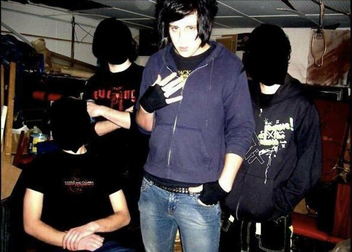 Teen in emo outfit posing with friends in garage, capturing an embarrassing blunder years moment.