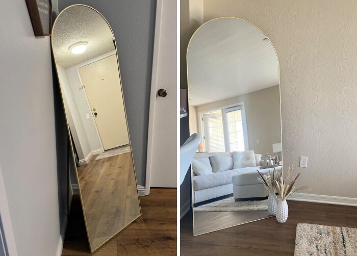Arched full-length mirror with gold frame on wooden floor, showcasing elegant decor and a cozy living room with expensive taste.