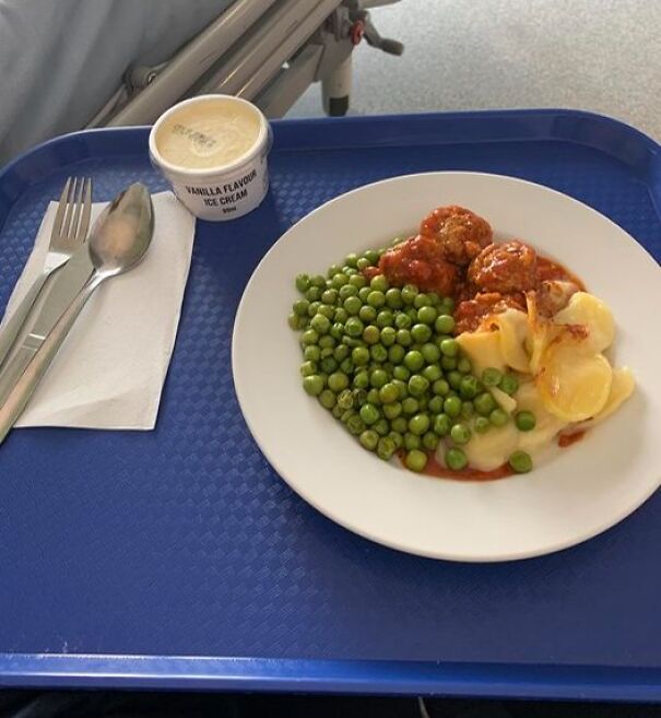 Hospital food tray with peas, meatballs in sauce, scalloped potatoes, and a cup of vanilla ice cream.
