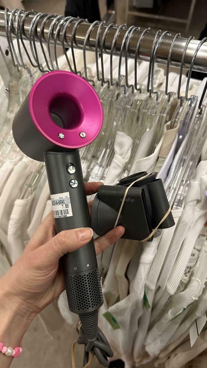 Thrift store find of a discounted, high-end hair dryer with pink accents held over clothing racks.