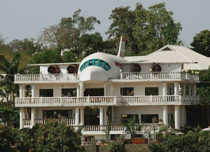 Unique bizarre building designed to look like an airplane integrated into a multi-story residential structure surrounded by trees.