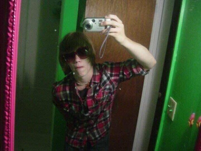 Young person taking a mirror selfie in a plaid shirt and sunglasses during their blunder years.