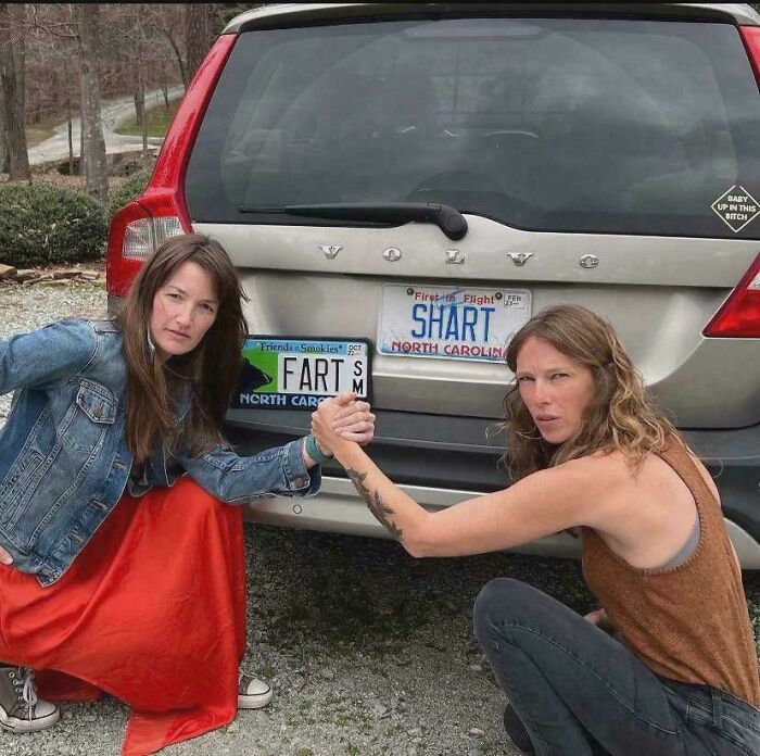 Two women posing with humorous license plates on a car, showcasing a fun real-life "Final Boss" moment.