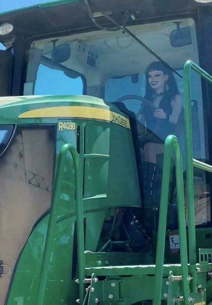 Person dressed in goth attire driving a large green tractor, an unexpected sight that makes people go 'hmmm'.
