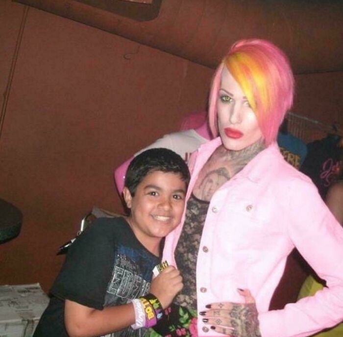 Young boy smiling with a person in colorful hair and pink jacket during blunder years.
