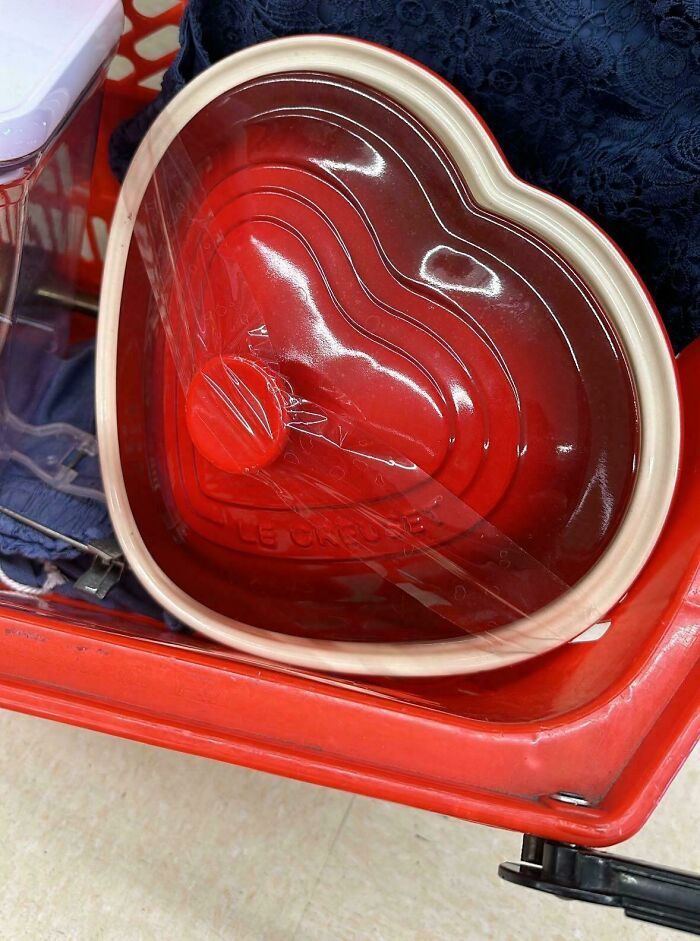 Heart-shaped red Le Creuset pot found while thrifting, nestled in a red shopping cart with blue fabric underneath.