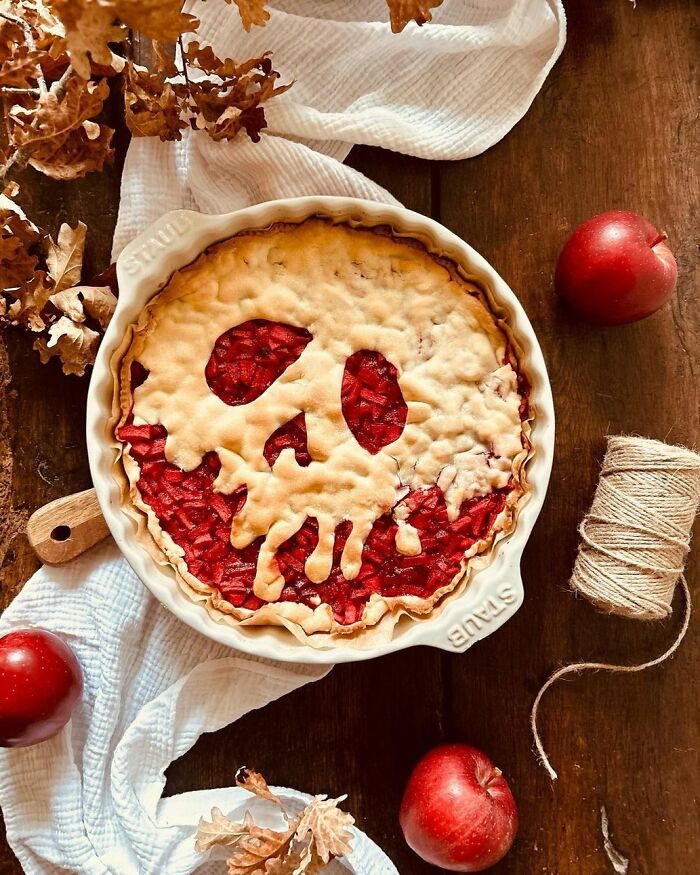 Halloween snack pie with skull-shaped crust design surrounded by autumn leaves and apples on wooden table