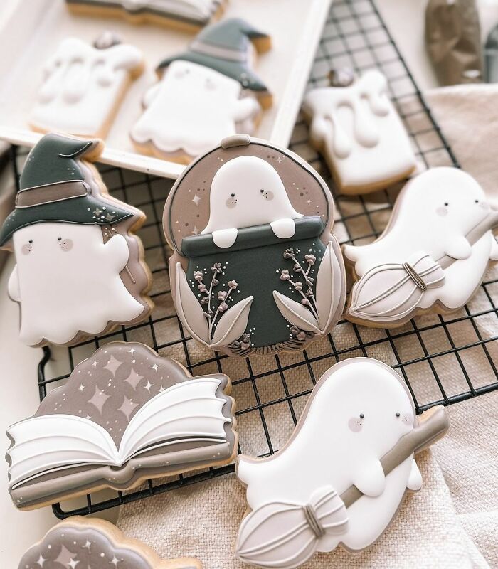 Decorated Halloween snacks featuring ghost and witch-themed cookies with detailed icing on a cooling rack.
