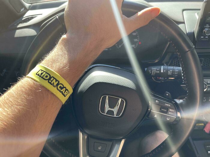 Padre conduciendo un auto con pulsera amarilla que dice Kid in Car, capturando momento divertido y tierno de paternidad.