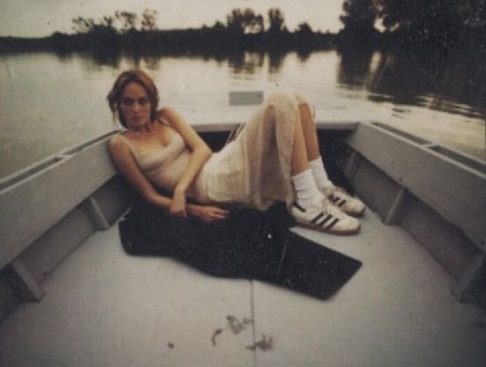 Person relaxing in a boat, wearing a dress and sneakers, capturing a wholesome ‘90s moment on water.