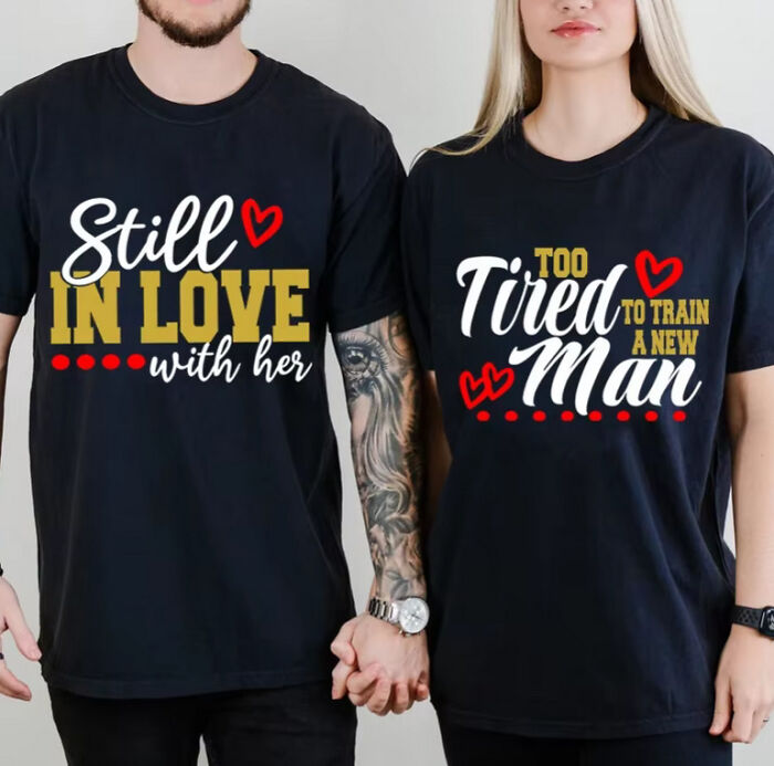 Couple wearing matching shirts with playful messages, hand in hand, expressing relationship dynamics.