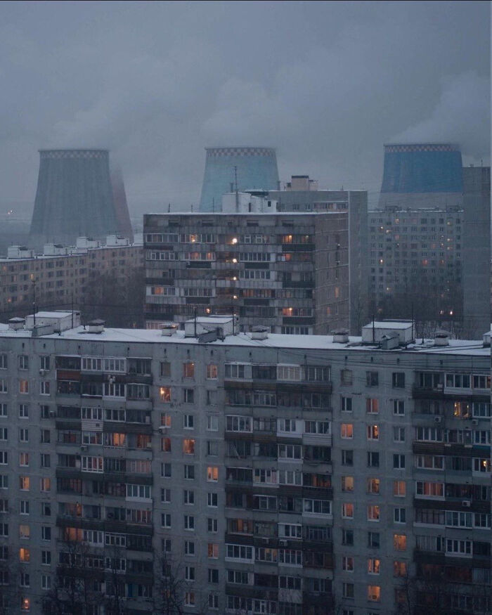 Urban landscape with gray buildings and smoking cooling towers in the background, depicting an industrial area.