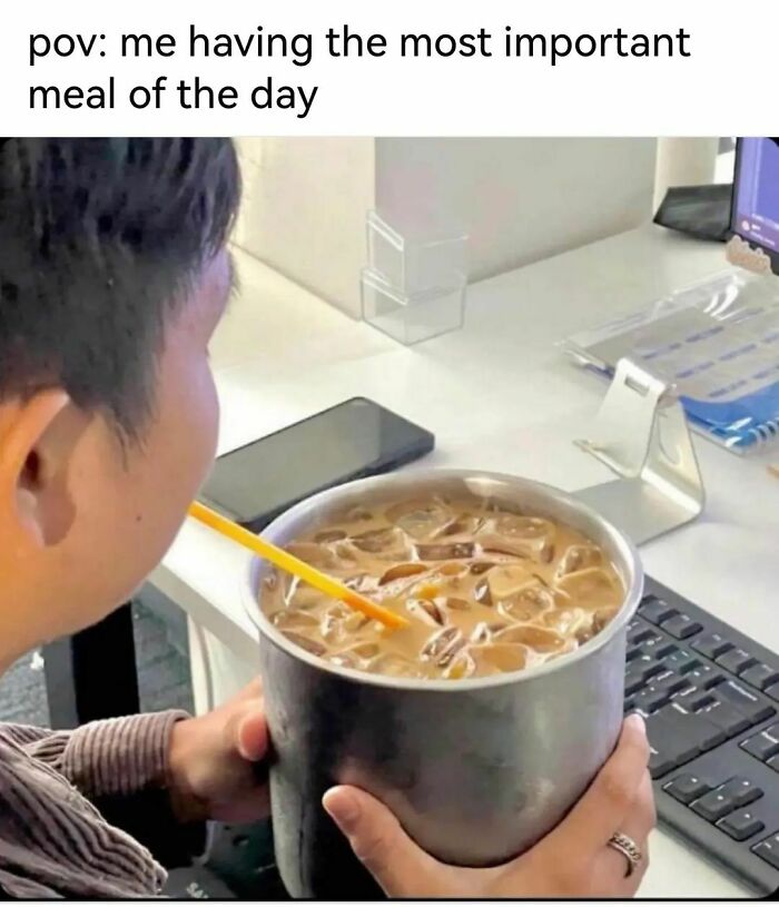 Person drinking from an oversized cup filled with iced coffee at a desk, relatable meme about important meals.