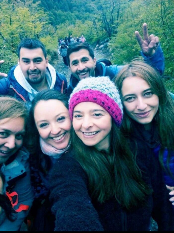 A group of people taking a selfie in nature, seamlessly merging with the background of lush green trees and a trail.