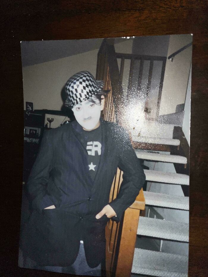 Young person in costume with a checkered hat and makeup poses near wooden stairs, showcasing blunder years style.