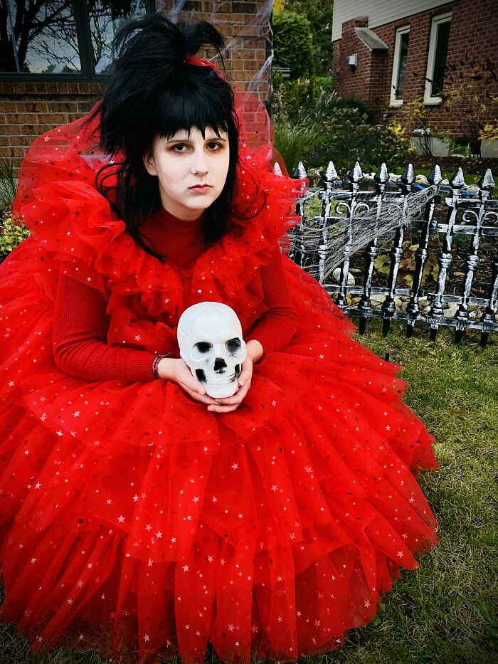 Child in elaborate red Halloween costume holding a skull, sitting outdoors for kids Halloween costume ideas that worked like magic.
