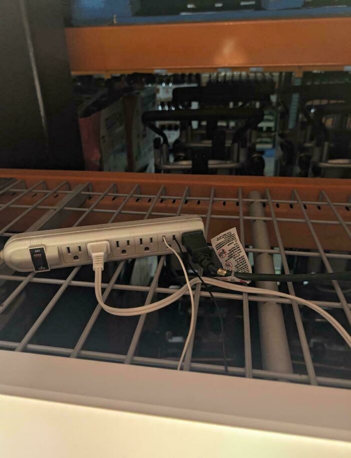 Power strip improperly placed on metal grating with cords tangled, showcasing a blatant safety protocol violation by employees.