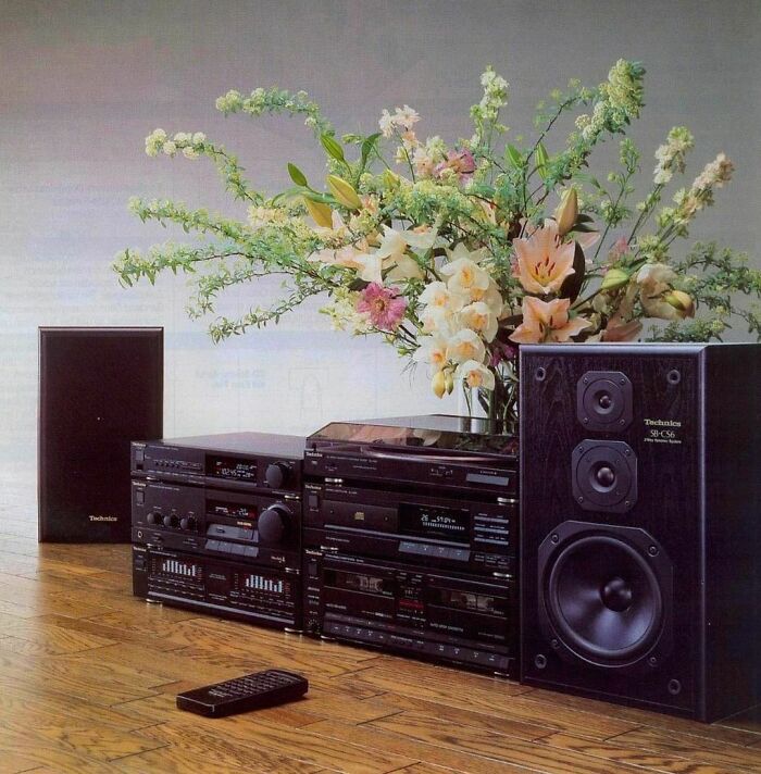 '90s stereo system with speakers and remote on a wood floor, flowers in vase.