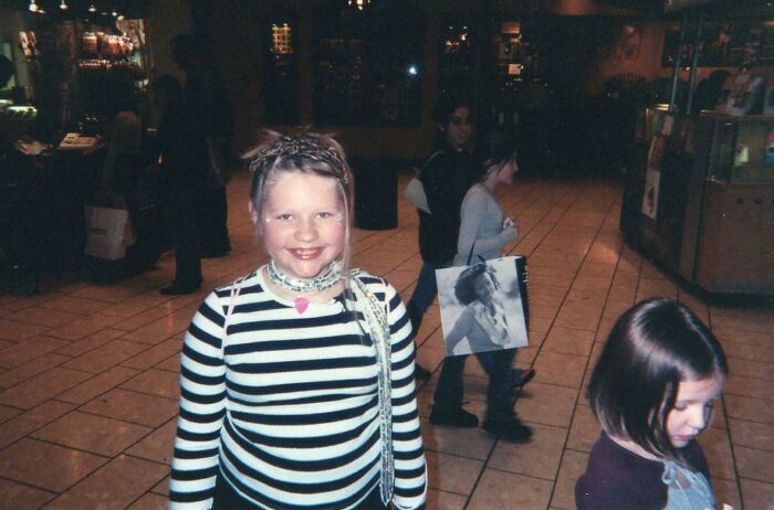 Child in striped shirt smiling in a mall, nostalgic blunder years moment.