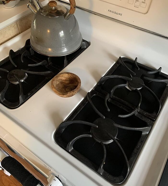White stove gas burners with black grates and a metal kettle, demonstrating genius hacks to conceal eyesores in the kitchen.