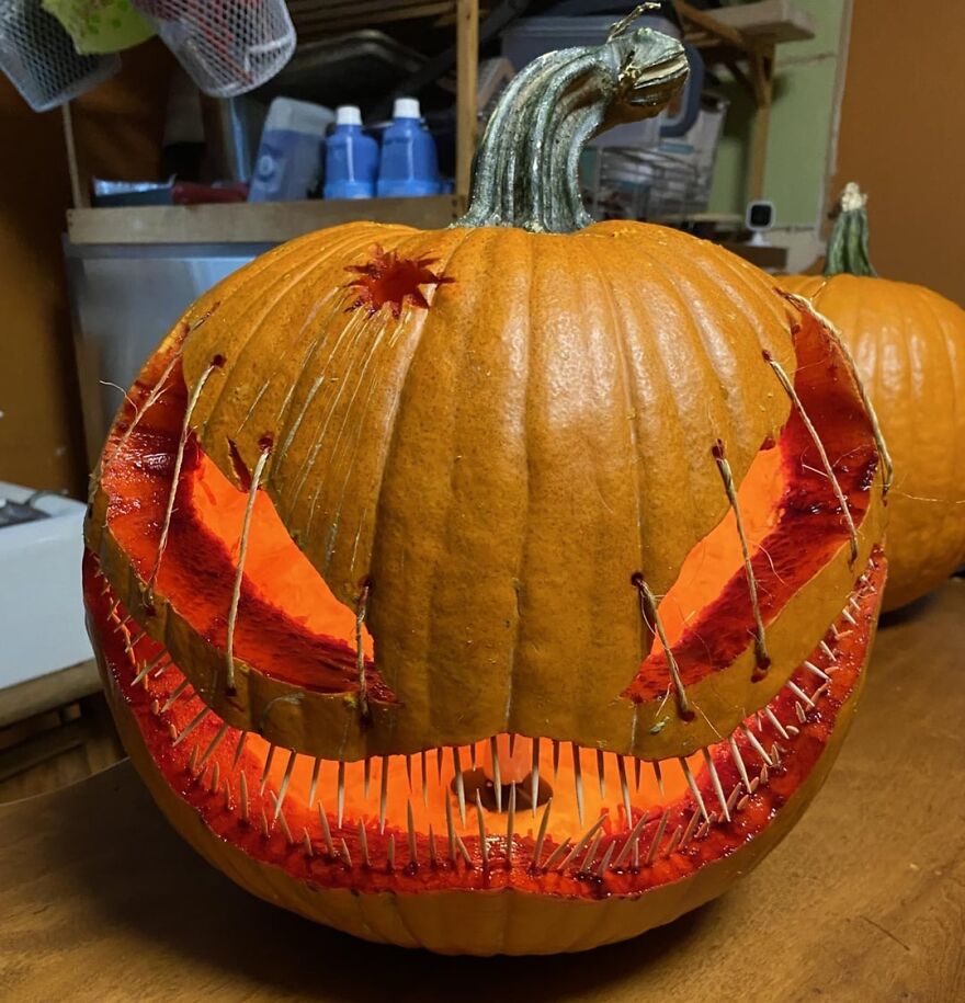 Pumpkin carving with spooky and quirky stitched mouth and eyes glowing from inside on a wooden table indoors